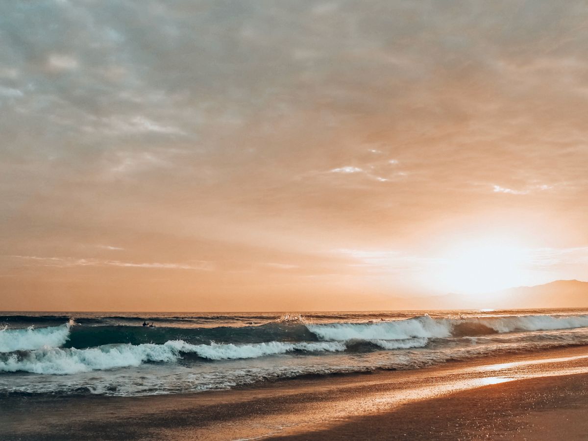 A serene beach scene at sunset, with gentle waves crashing onto the shore under a golden sky, creating a tranquil and picturesque atmosphere.