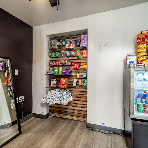 A small convenience area with snacks on shelves, a fridge with drinks, and a mirror on the left side.