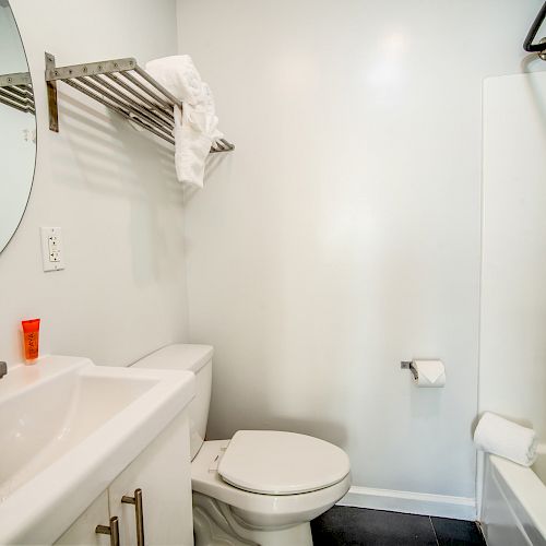 A bathroom with a sink, mirror, toilet, tub, shower, towel rack with a towel, and a small red item on the sink.