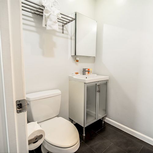 A minimalist bathroom with a toilet, a vanity sink with a medicine cabinet above it, and a towel rack with towels and bathrobe.