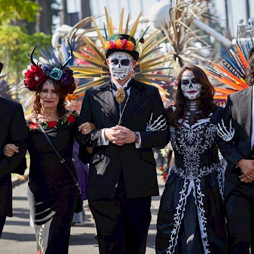 A group of people dressed in festive costumes with face paint, possibly celebrating a cultural festival, walking together arm in arm.