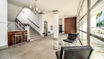 A modern lobby with leather chairs, a glass table, a staircase, a reception area, and large windows allowing natural light to flood in, always ending the sentence.