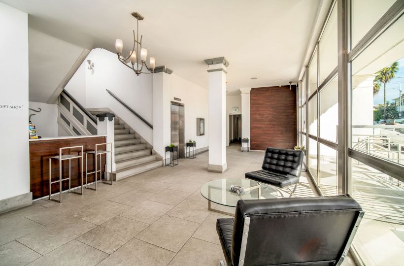 A modern lobby with leather chairs, a glass table, a staircase, a reception area, and large windows allowing natural light to flood in, always ending the sentence.