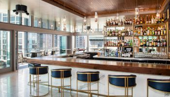 A chic, modern bar with a wooden countertop, stylish bar stools, and an extensive selection of liquor bottles displayed on shelves.