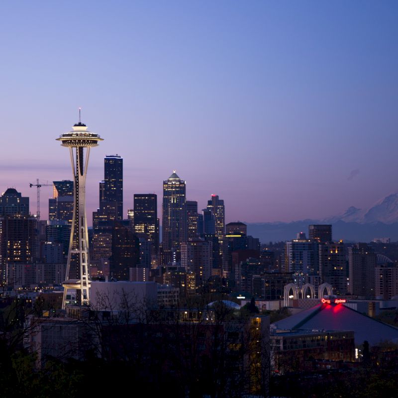 A twilight view of Seattle's skyline, featuring the illuminated Space Needle and Mount Rainier visible in the background, with the city's buildings.