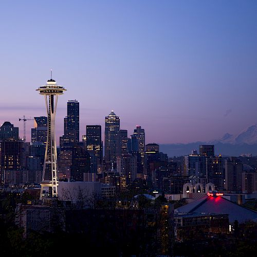 The image shows the Seattle skyline at dusk with the iconic Space Needle and Mount Rainier in the background.