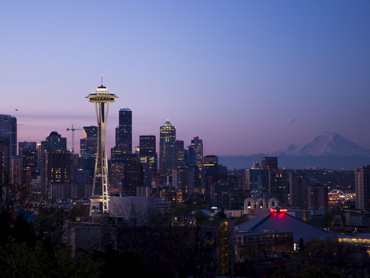 The image shows the Seattle skyline during twilight, featuring the Space Needle prominently and Mount Rainier in the background.