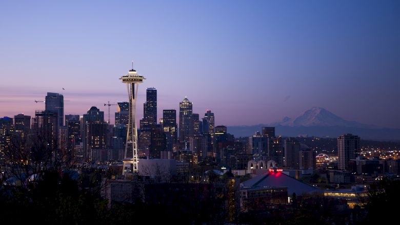 The image shows the Seattle skyline during twilight, featuring the Space Needle prominently and Mount Rainier in the background.