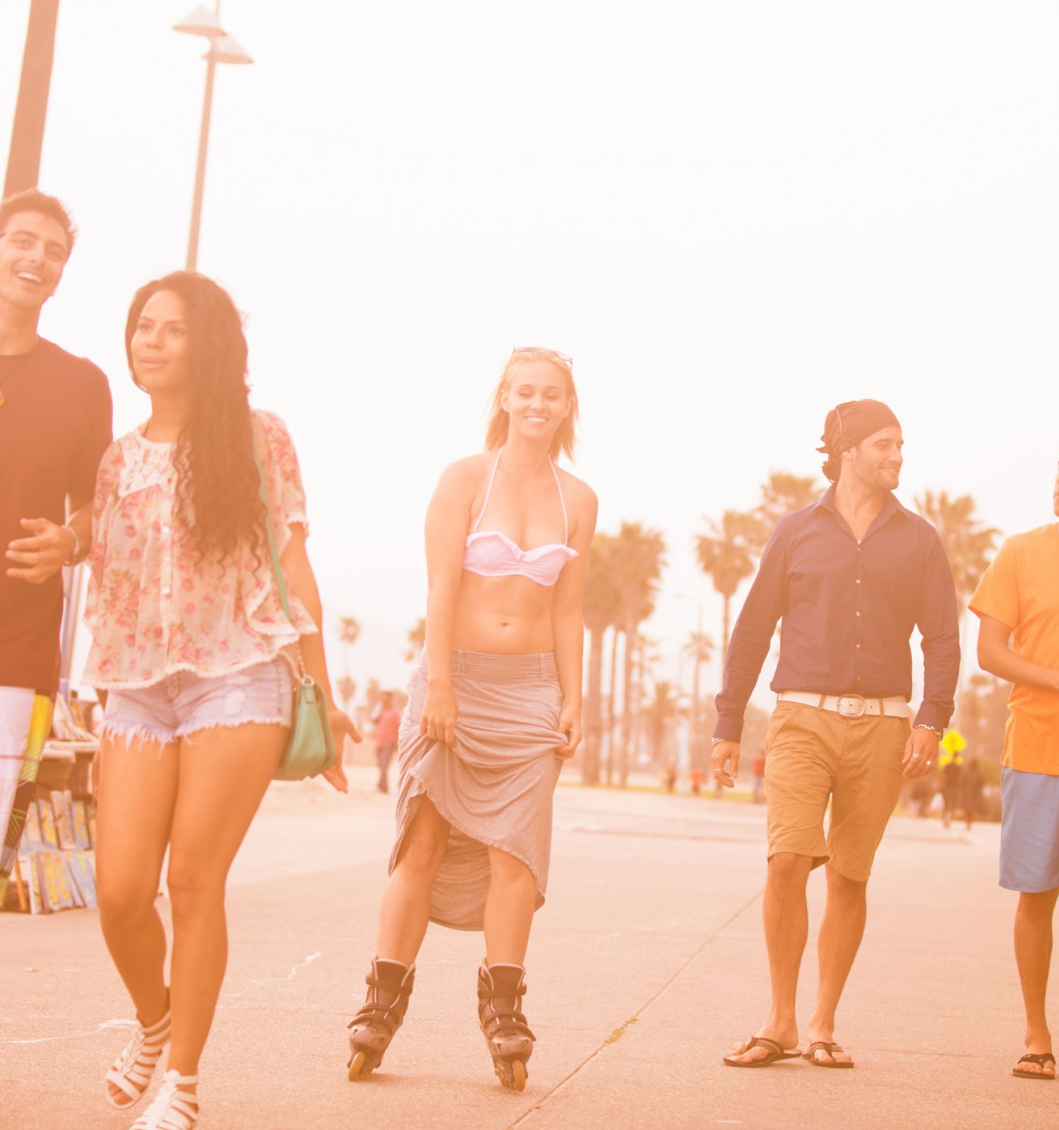 A group of five people walking together near the beach on a sunny day, with palm trees and buildings in the background.